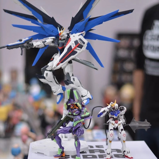 MG Freedom Gundam, an Evangelion Unit-01 kit and HG Gundam Barbatos posed on The GEAR Store's stall box at a convention