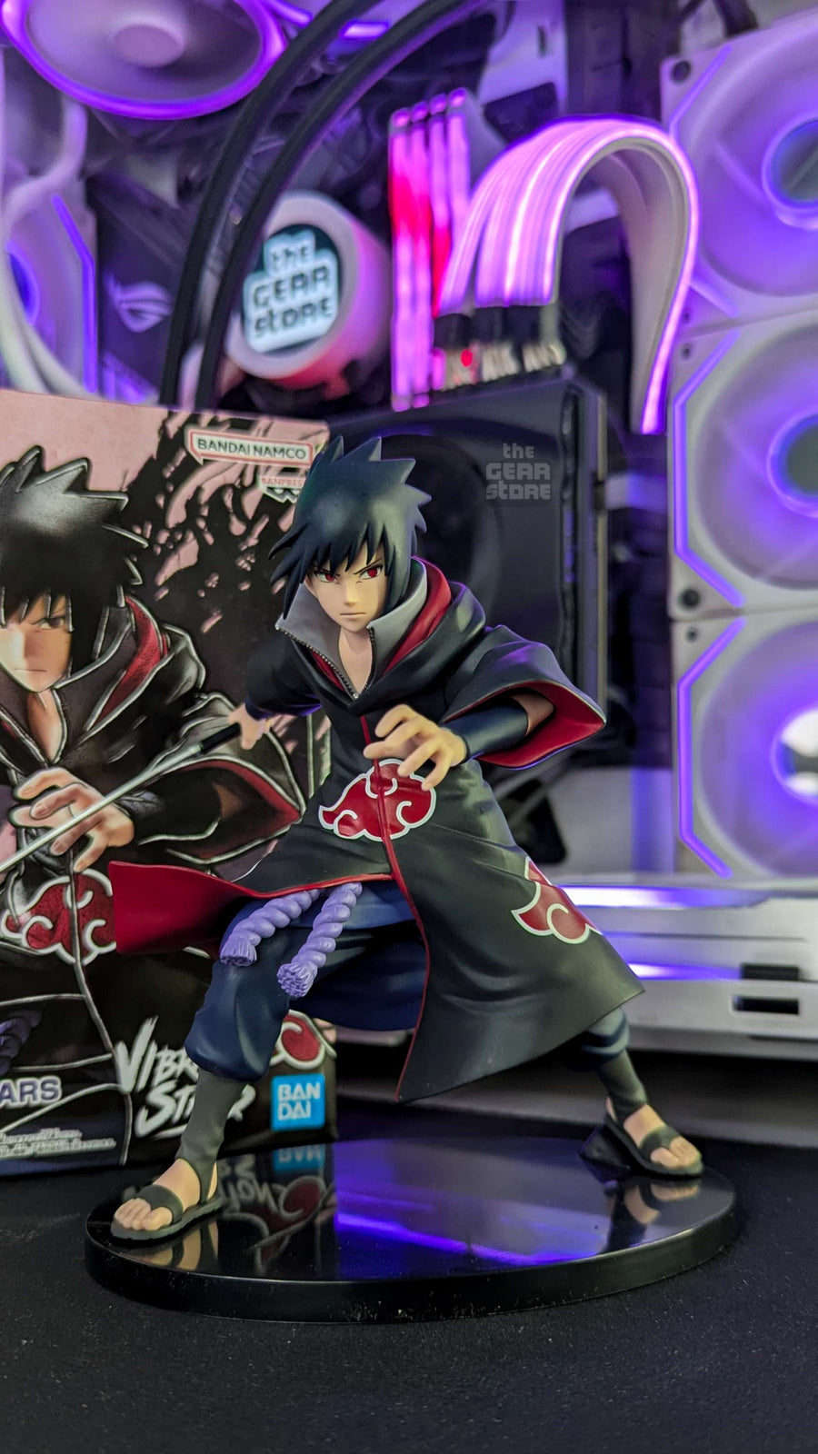 A Sasuke Uchiha figure in Akatsuki robes on The GEAR Store's desk, the RGB-lit PC behind it