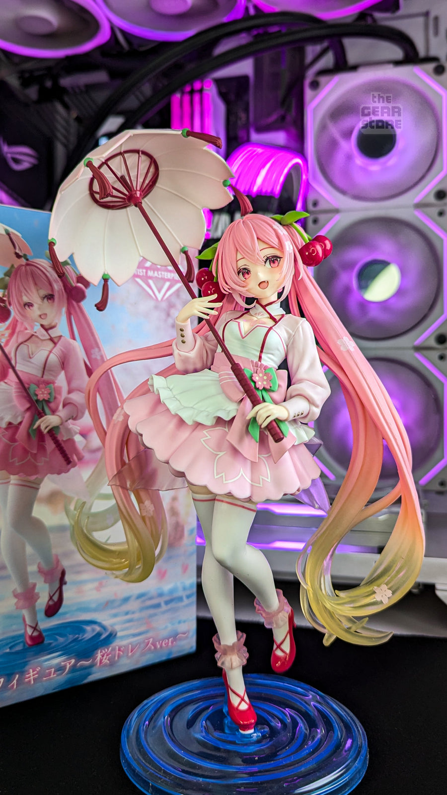 A Sakura Miku figure with a parasol on The GEAR Store's desk, the RGB-lit PC behind it